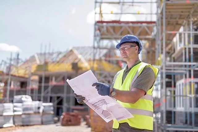 A construction worker looking at plans beside a building.