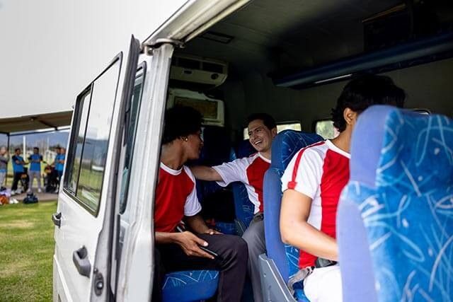 Team members in a van, with one smiling and talking while others sit nearby.