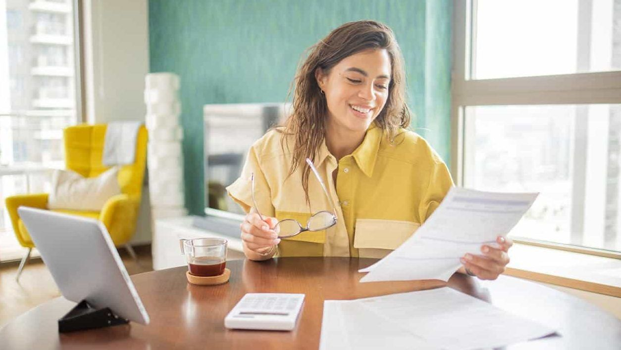 Person sat at a a table in their living room smiling while looking at paper work