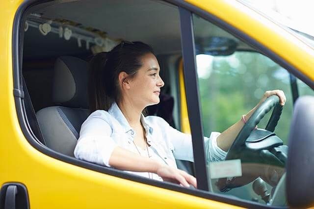 A woman smiling while driving a bright yellow van on a sunny day.
