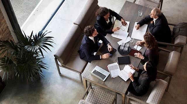 Five people wearing business suits are engaged in conversation while sitting around a table.