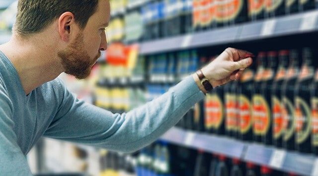 Man reaching for a bottle in a grocery store, surrounded by various beverages.