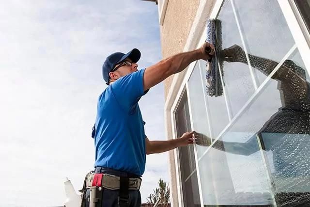 A window cleaner in uniform, cleaning a window with a squeegee.