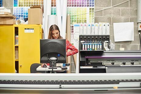 Woman working on a computer in a print shop with color samples and printing supplies.