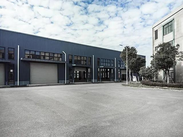 Industrial building with blue panelling, garage doors, and greenery, under a cloudy sky.