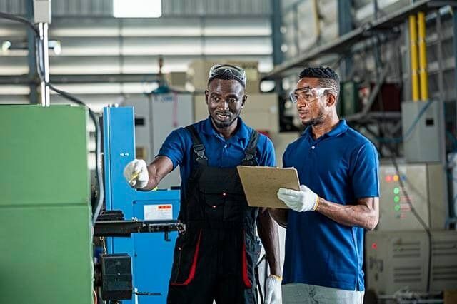 Two men discussing an engineering task in a manufacturing workshop with safety gear on.