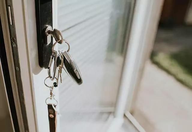 Keys inserted into a door lock, with green grass visible outside.