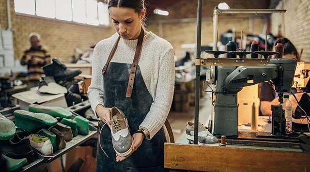 Person inspecting a shoe in a workshop with shoemaking tools and machinery in the background.