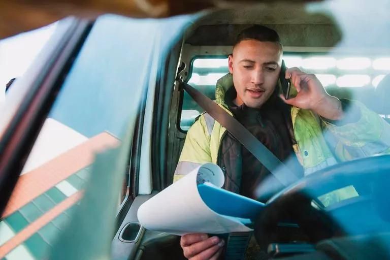 Contractor sitting in the driver’s seat of a van, talking on the phone and looking over some paperwork.