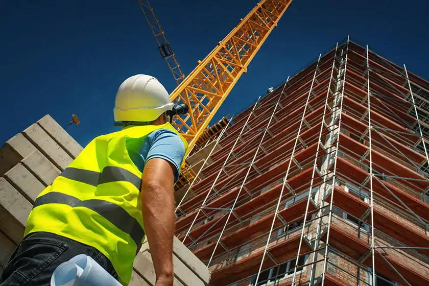 A construction worker stands in front of a building, with scaffolding visible in the background, showcasing ongoing construction work.