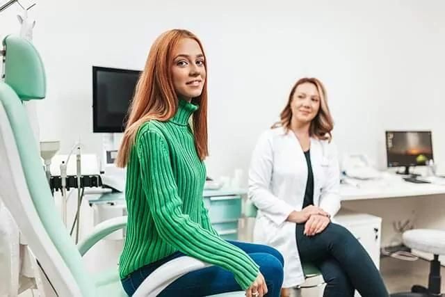 A woman is sitting on a medical chair while an audiologist is sitting at their desk.