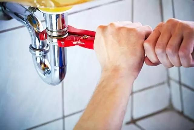 A close-up at the hands of a plumber using a wrench under a toilet sink.