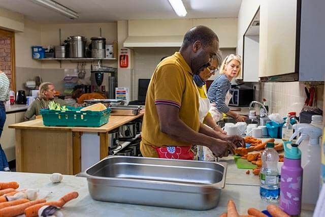 People preparing food in a community center kitchen, chopping vegetables and using kitchen items.