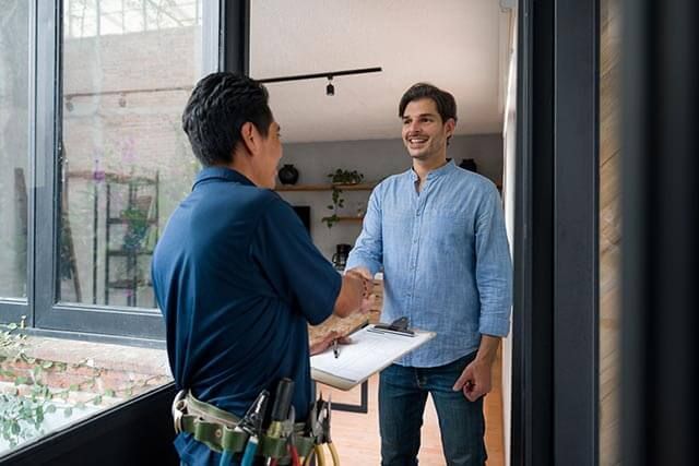 Contractor shaking hands with a customer outside a house, both smiling in a friendly, professional exchange.