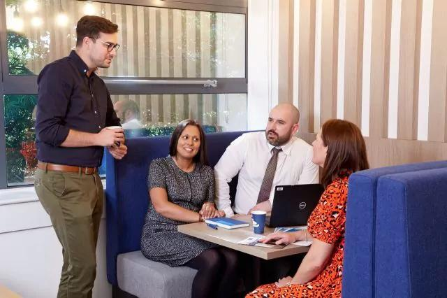 Four people having a work meeting in a booth, with a laptop and notebooks.