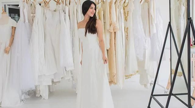 Woman in a white wedding dress standing before racks of dresses in a wedding dress store.