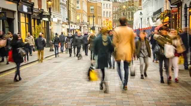 A lively street scene with shops on either side and pedestrians strolling along the sidewalk.
