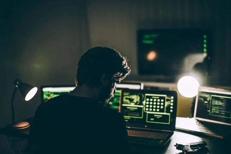 Silhouette of a person stat at a desk working on a laptop with a spotlight.