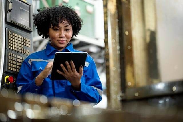 Female Engineer in blue uniform using a tablet beside industrial machinery in a factory.