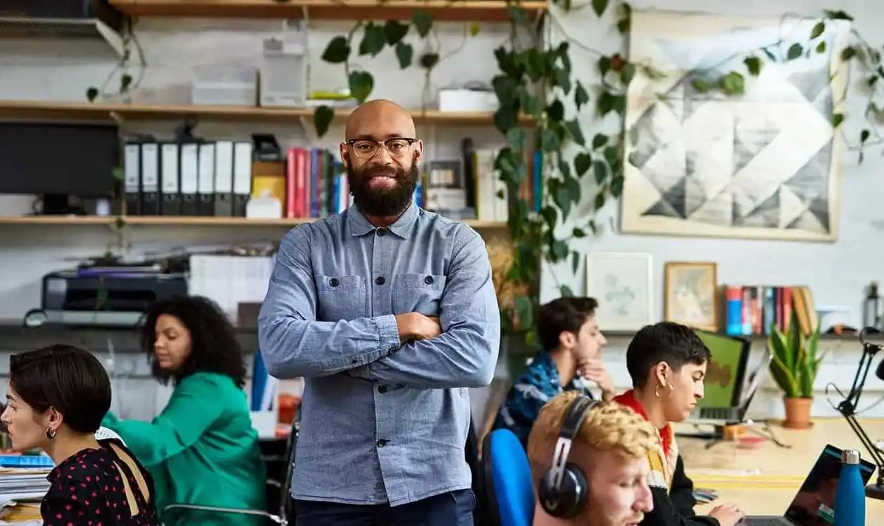 A man stands before a group of people focused on their computers in a collaborative workspace.