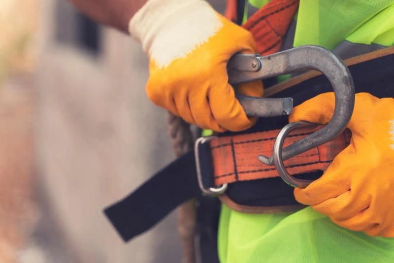 A worker wearing a safety harness, fastening a hook onto the harness belt to ensure construction site safety