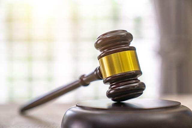 Close-up of a judge’s gavel resting on a sound block in a courtroom with blurred background.