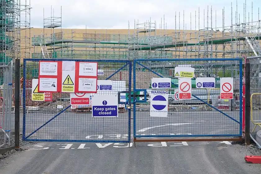 A blue gate with numerous signs attached, marking the area as a closed building site.