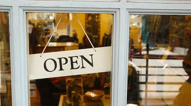 Close-up of a shop window with a hanging “Open” sign. The interior is warmly lit with various items and shelves in the background