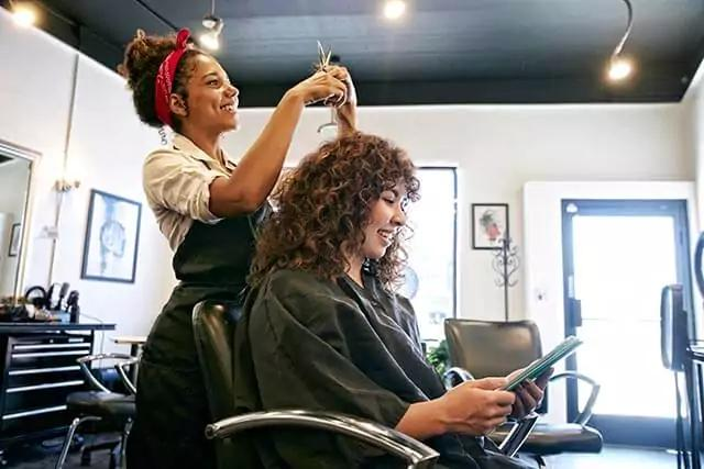 A hairstylist trims a woman's hair, showcasing a professional salon environment.