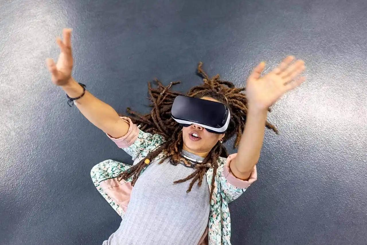 A woman with dreadlocks is immersed in a virtual reality experience, wearing a VR headset. 