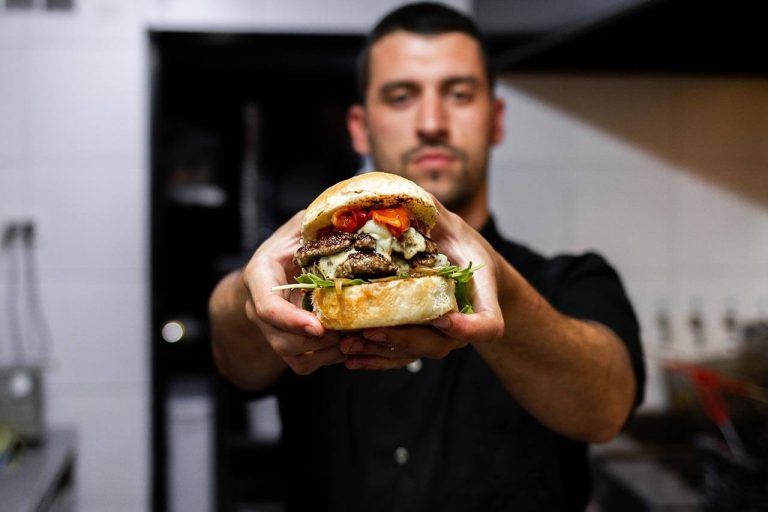 Chef holding a large sandwich. A close-up of the sandwich, while the background is blurred.