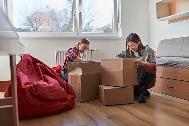 Two students unpacking boxes in a room with wooden floors and a red beanbag.