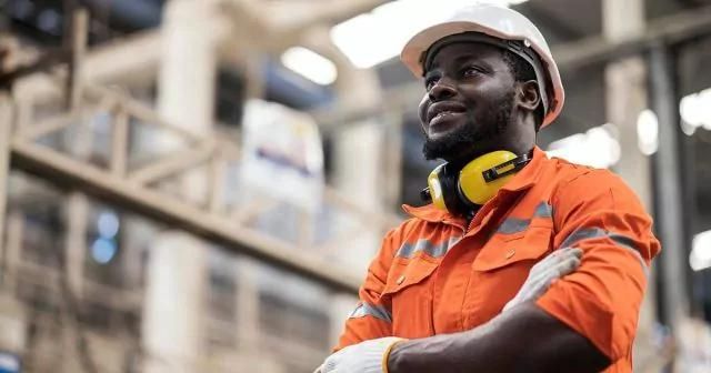 Worker in safety gear standing confidently in an industrial setting.