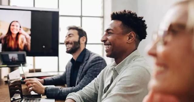 Three people in an office meeting, smiling while on a video call together.