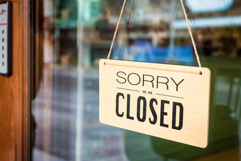 Close-up of a “Sorry, We’re Closed” sign hanging on a glass door with a blurred indoor background.