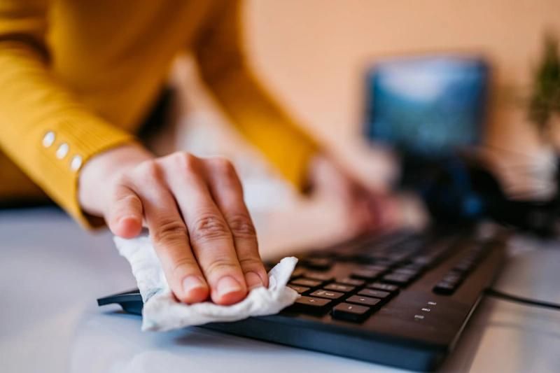 Person wiping their keyboard clean with a wipe