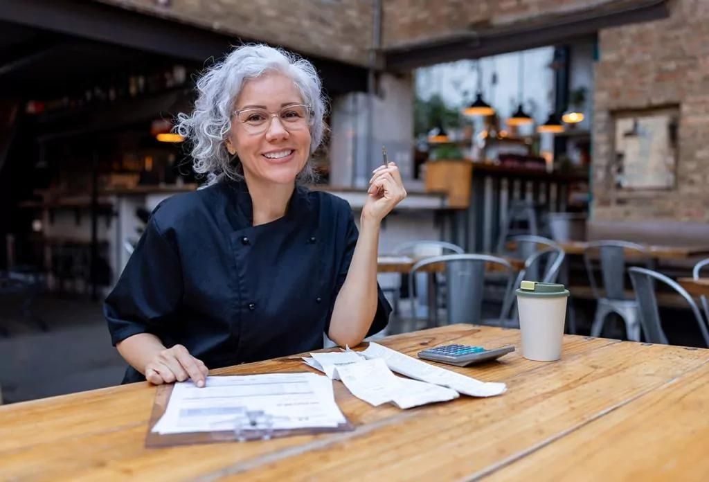 A woman at a table with coffee and a menu, focused on her business and the impact of energy bills.